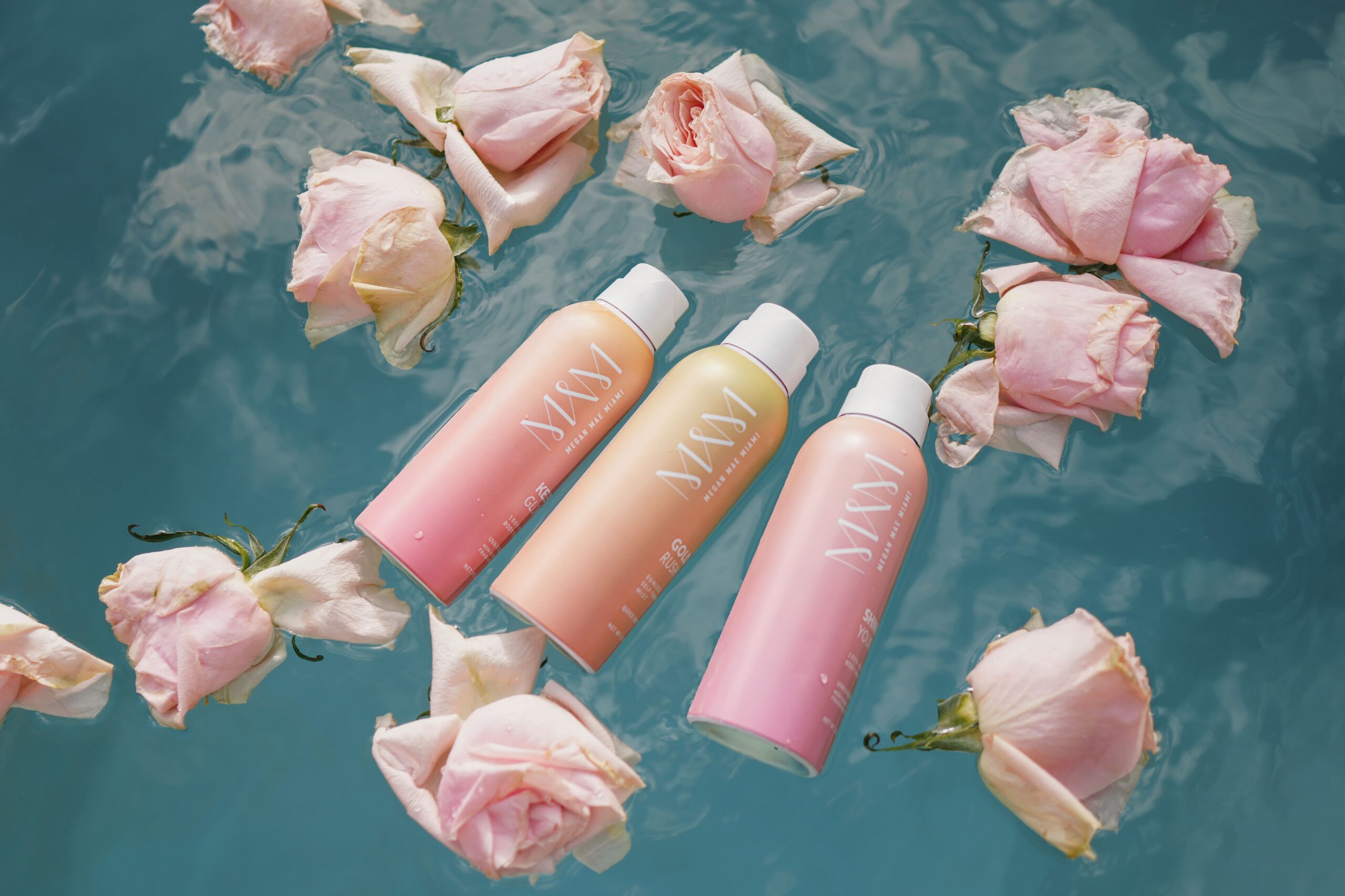 bottles of Megan Mae Miami® suncare floating in pool with roses